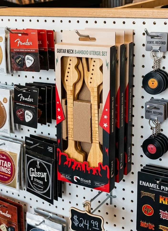 The Guitar Neck Bamboo Utensil Set hanging in its printed retail box on a music shop pegboard, in an accessories bay beside guitar picks and strings